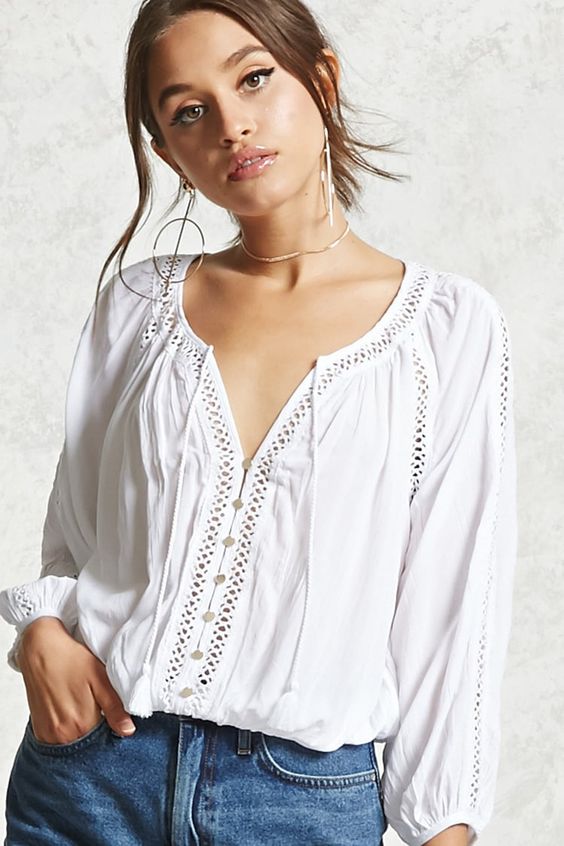 A woven peasant top featuring a V-neckline with tassels, a mock button placket, long sleeves, crochet cutout detailing throughout, and an elasticized hem.